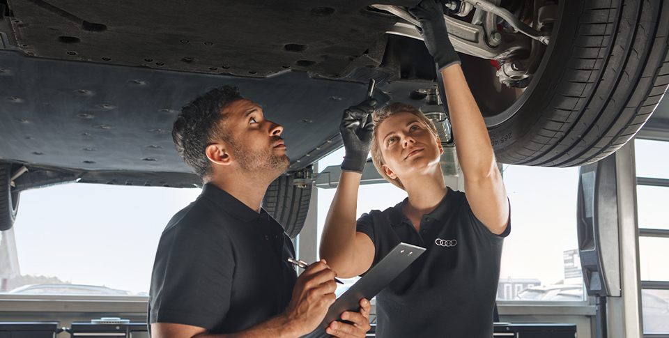 Zwei Personen schauen sich ein Auto auf der Hebeb&uuml;hne von unten an