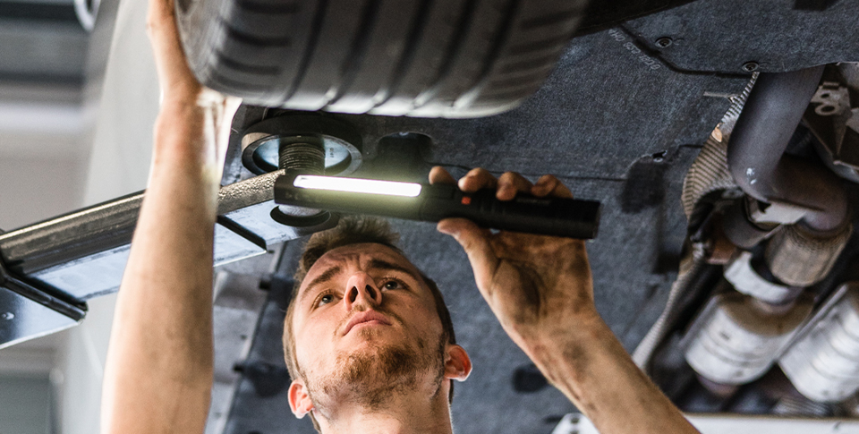 Mechaniker schaut sich ein Auto auf der Wagenb&uuml;hne von unten an